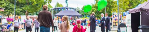 Kesäpäivänä ihmisiä kävelemässä Hämeenpuiston Puistofiesta-tapahtumassa. Etualalla kulkee mies kahden lapsen kanssa. Lapsilla on vihreät ilmapallot.