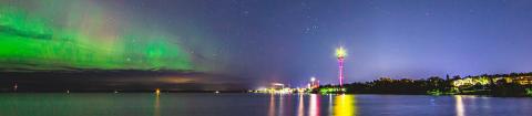 A night view from Lake Näsijärvi, green northern lights in the sky, the Näsinneula and the city lights shining in the distance.
