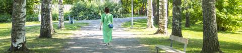 Vihreäpukuinen nainen kulkee kesällä Kaukajärven puistokujalla.