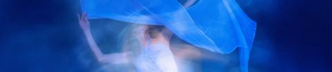A person in a white dress dances with a flowing blue fabric against a dark blue background.