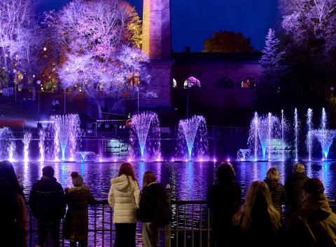 Valotaideteos violetin sävyissä vesisuihkuineen Tammerkoskessa, etualalla yleisöä sitä katsomassa.