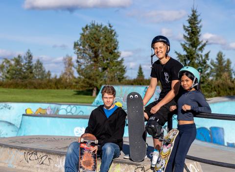 Kolme nuorta rullalautoineen istuskelee skeittirampilla.