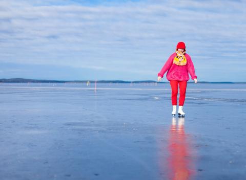A person dressed in red skates on the frozen lake.
