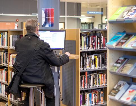 Henkilö istuu tietokoneen ääressä kirjastosalissa