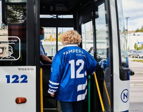 Suomen kannustuspaita päällä oleva nainen astuu sisään bussiin.