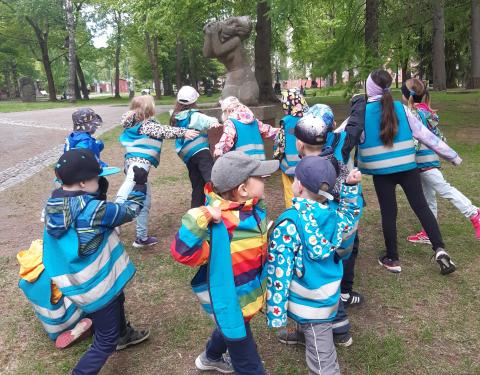 Joukko lapsia on patsasmaisissa asennoissa Aleksanterin kirkkopuiston Suru-veistoksen vieressä.