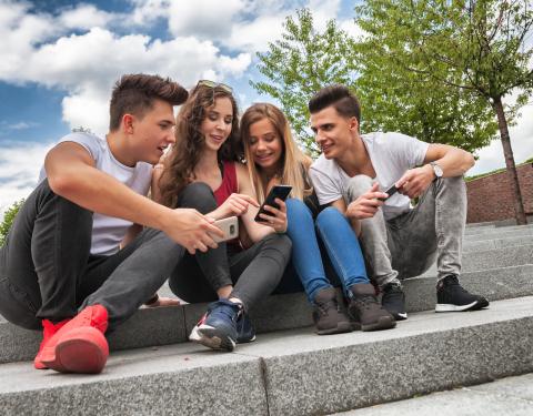 Neljä nuorta istuvat kivisillä portailla. Kaksi selaa kännykkää ja muut katsovat.