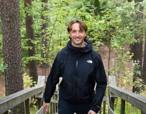 Smiling man standing at the top of wooden stairs with a lush forest around him.