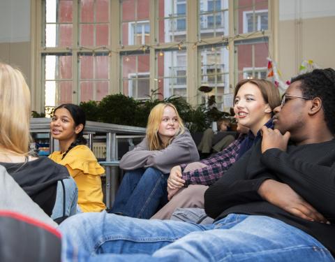 Nuoria henkilöitä istumassa sohvilla, taustalla ikkuna.