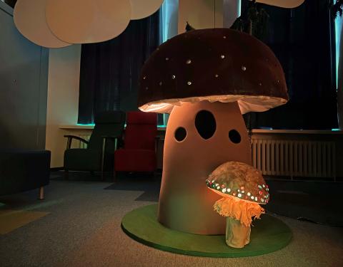 Iso ja pieni käsin tehty sieni, joiden hatut hohtavat valoa. 