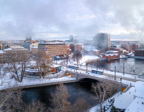 Buses and people pass over the Hämeensilta bridge over Tammerkoski rapids. There is snow on the ground.
