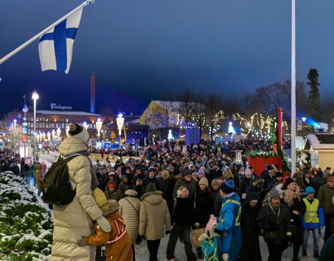 Ihmisjoukkoa illan hämärässä torilla. Suomen lippu liehumassa.