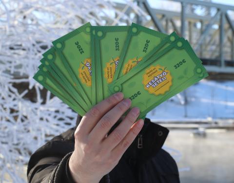 Henkilö esittelee kädessään olevia Kesätyöseteleitä talvisen Tammerkosken rannassa.