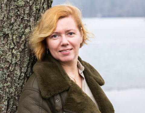 Henkilö nojaa puunrunkoon ja katsoo suoraan kameraan.