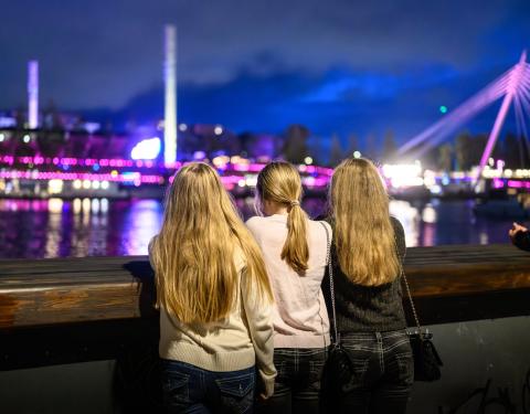 Kolme nuorta nojaa kävelysiltaan selät kameraan päin iltaisessa Tampereessa.