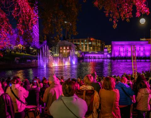 A gathering of people watching a Dancing waters show at the Tammerkoski at night.