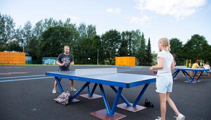 An adult and a child play ping pong outdoors.