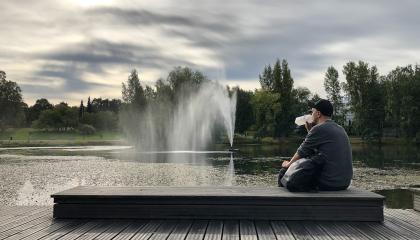 Henkilö istuu laiturilla, juo vettä ja katselee suihkulähdettä Sorsapuistossa.