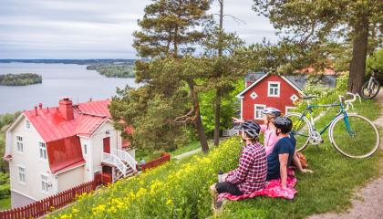 Kolme henkilöä pyöräilykypärät päässä katselee Pyhäjärvelle Pispalanharjulla, maisemassa myös puutaloja ja polkupyöriä.