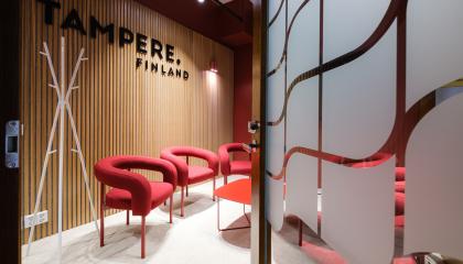 Kuvassa näkyy avattu ovi, jonka takana on neuvotteluhuone. Huoneessa on punaisia nojatuoleja ja sen seinällä lukee tampere.finland.