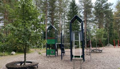 Tummansininen kiipeilyteline ja liukumäki puun vieressä Toispuolisenpuistossa.