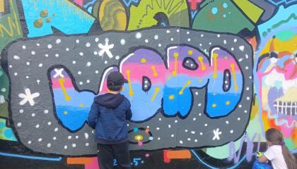 Graffiti seinä, jonka edessä kaksi lasta maalaamassa.