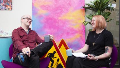 Kaksi ihmistä istuu kahvikupit kädessä vastakkain. 