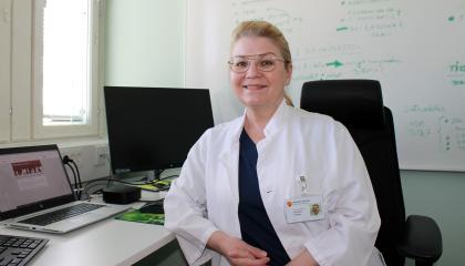 Anna Maria Heikkinen työpöytänsä ääressä valkoinen hammaslääkärin takki päällään.