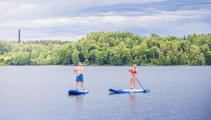 Kaksi henkilöä sup-lautailee järvellä.