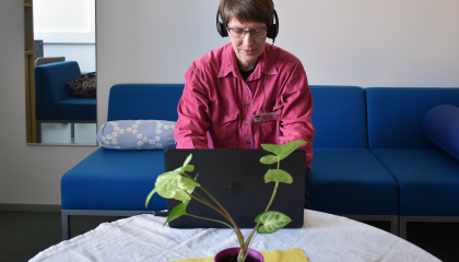 Henkilö istuu sohvalla tietokoneen ääressä kuulokkeet päässään.