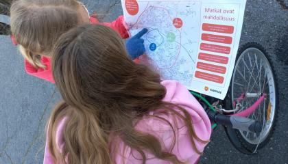 Kaksi koululaista tutkii karttaa, kuvassa polkupyöriä.