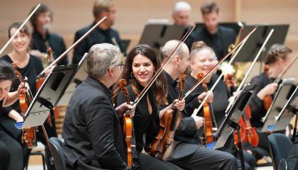 The Tampere Philharmonic Orchestra&#039;s musicians sitting with their instruments in the concert hall, María Garcia in the middle.
