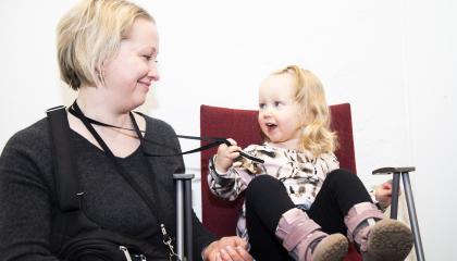 Äiti ja lapsi katsovat toisiaan hymyillen. Lapsi pitää kädessään äidin henkilökorttia.