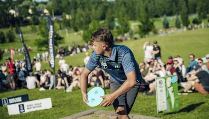 Henkilö frisbeegolfaa yleisön edessä.