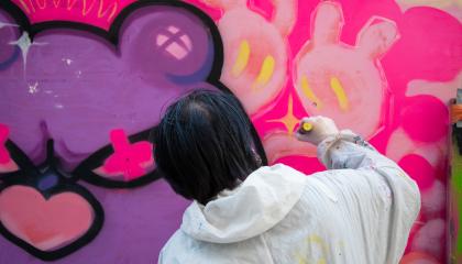 Nuori henkilö maalaa valkoisessa haalarissa graffitia.