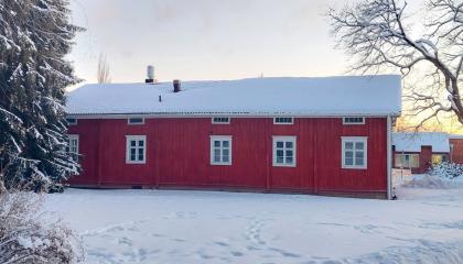 Talvisessa maisemassa puuverhoiltu punainen yksikerroksinen maatalo, Hatanpään pirtti, jonka yhdellä sivulla on viisi ikkunaa.