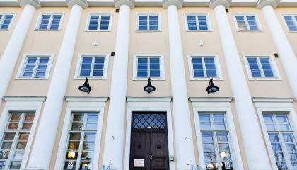 Vaalenkeltaisen ison rakennuksen julkisivua koristaa valkoiset pylväät. Julkisivulla on paljon ikkunoita.