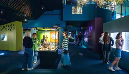 Hämärässä sinertävässä museotilassa on runsaasti ihmisitä tutkimassa valaistuja vitriineitä. 