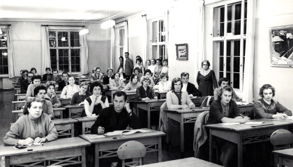 Henkilöt istuvat pulpeteissa luokkahuoneessa.