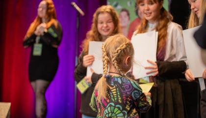 Lapsi ottaa vastaan kunniakirjaa kolmelta massiraadin jäseneltä