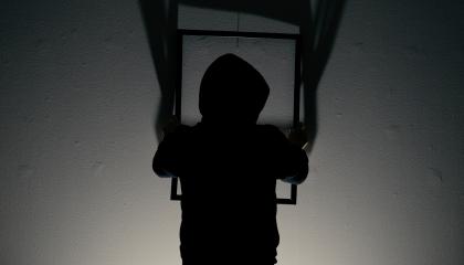 Tumma hahmo ripustaa tyhjää kehystä vaalealle seinälle.