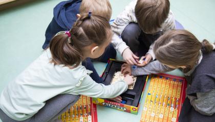 Neljä lasta istuu ringissä ja pitää käsiä keskellä päällekkäin.