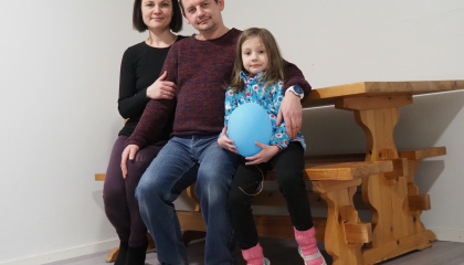 Kolmihenkinen perhe istuu pöydän äärellä. Lapsella on kädessä sininen ilmapallo.