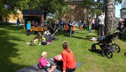 Eri ikäisiä istumassa puistossa. Kuvan etualalla aikuinen ja lapsi viltin päällä.