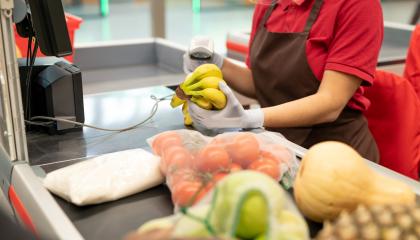 Kaupan kassahihnalla on erilaisia hedelmiä ja vihanneksia. Kassatyöntekijä, josta näkyvät vain kädet, on lukemassa niiden hintoja.