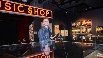 Museotyöntekijä valokuvaaja Saarni Säilynoja poseeraa Vapriikin Manserock-näyttelyssä työvälineensä kanssa.