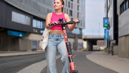 Nuori nainen sähköpotkulaudan kanssa katselee ympäristöä