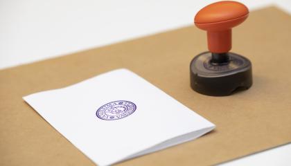 Valkoinen äänestyslippu ruskealla alustalla ja vieressä leimasin.