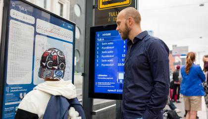 Mies ja poika tutkivat aikatauluja pysäkillä.