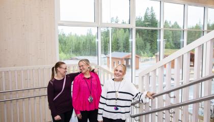 Kolme naista seisoo portaikossa rinnakkain. Taustalla ikkunoista näkyy metsä.